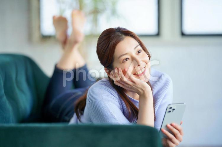 ソファーの上に寝そべってスマートフォンを使う女性 女性,日本人,1人の写真素材