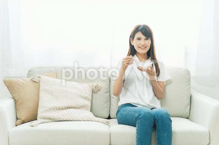 ソファでヨーグルトを食べる女性（笑顔） ヨーグルト,乳酸菌,菌活の写真素材