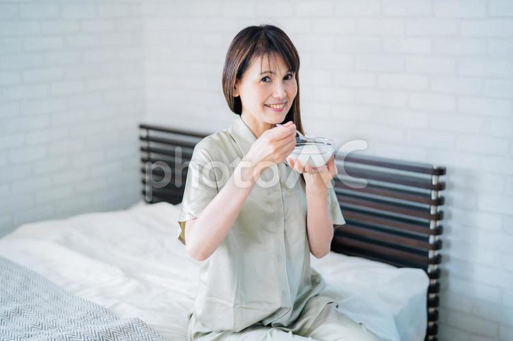 寝室でヨーグルトを食べるミドル世代の女性（笑顔） ヨーグルト,乳酸菌,菌活の写真素材