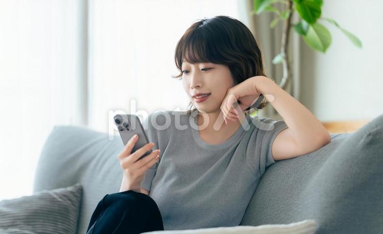 ソファに座ってスマホを使う笑顔の女性 女性,スマホ,スマートフォンの写真素材