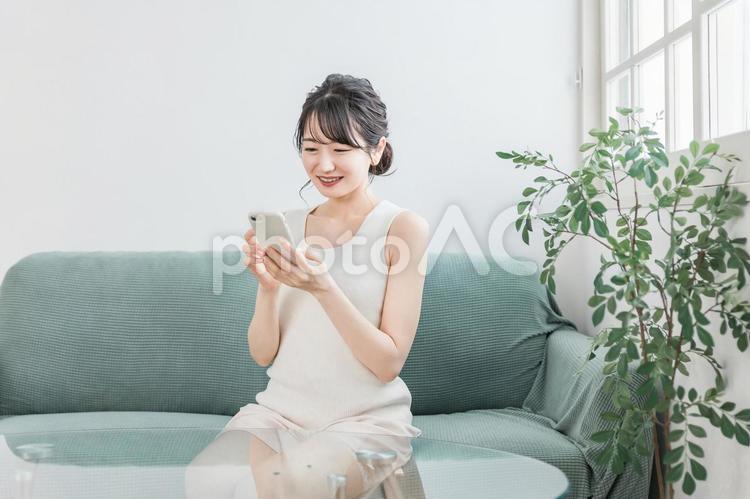 家でリラックスしながらスマホを使う女性 スマホ,アプリ,snsの写真素材