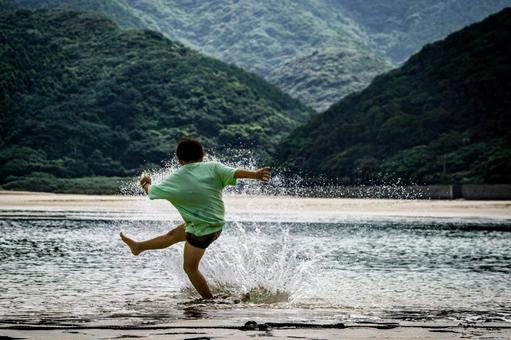 <素材>夕暮れの海で水遊びをする男の子 <素材>夕暮れの海で水遊びをする男の子の写真