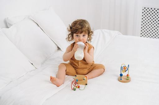 カメラ目線でベッドに座りミルクを飲む子供 カメラ目線でベッドに座りミルクを飲む子供 赤ちゃん,哺乳瓶,ミルクの写真素材