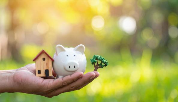 ブタの貯金箱と家の模型を持つ男性の手  ブタの貯金箱と家の模型を持つ男性の手の写真