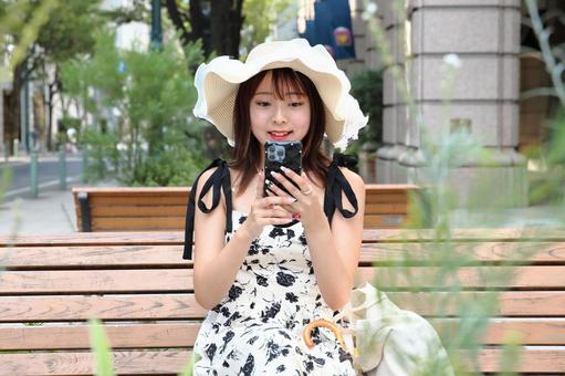 ベンチでスマホを見る女性 ベンチでスマホを見る女性の写真