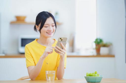 笑顔でスマホを操作する黄色の服の女性 女性,スマートフォン,持つの写真素材