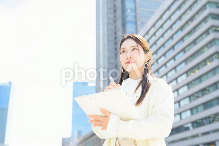 ビル街でバインダーを持って微笑む女性 バインダー,アンケート,キャリアウーマンの写真素材