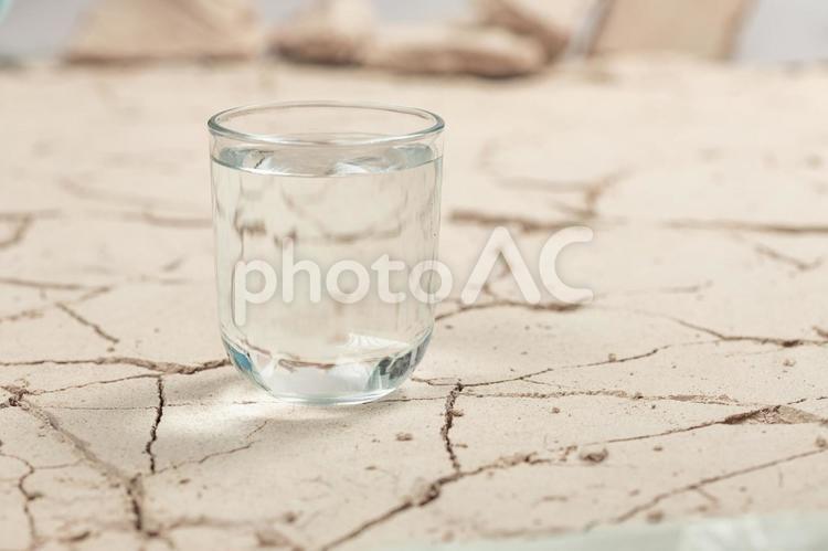 ひび割れた土の地面とグラスの水 温暖化,水不足,乾燥の写真素材
