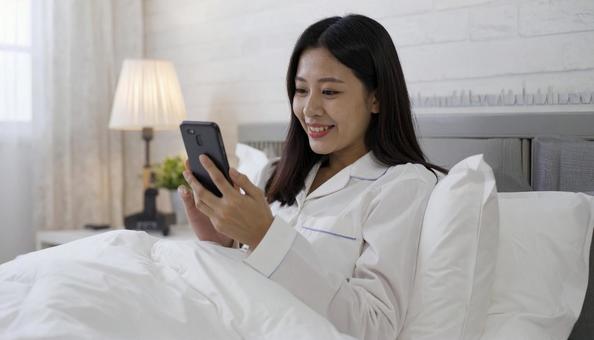 ベッドルームでスマホを見る日本人女性 ベッドルームでスマホを見る日本人女性の写真