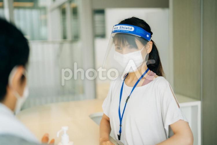 スポーツジムの受付をする女性（マスク・フェイスシールド） スポーツジム,受付,スタッフの写真素材