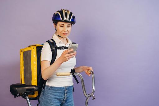 自転車を押してスマートフォンを見ているフードデリバリーの女性 配達,フードデリバリー,デリバリーの写真素材
