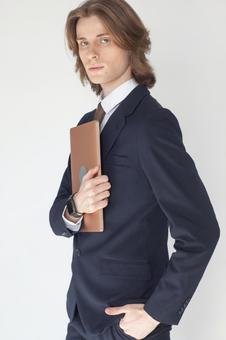 ノートパソコンを抱えてポケットに手を入れているカメラ目線のスーツの男性 男性,外国人,欧米人の写真素材