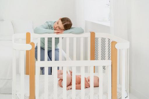 ベビーベッドの脇で寝ている女性 ベビーベッドの脇で寝ている女性 親子,女性,赤ちゃんの写真素材