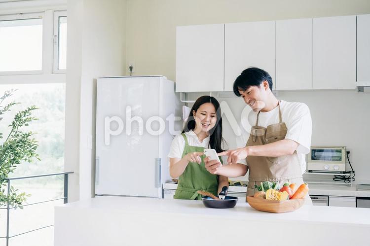 スマホを見ながら料理する男女（笑顔） 料理,家事,レシピの写真素材