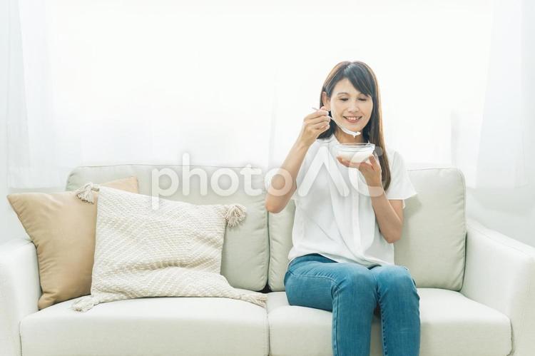 ソファでヨーグルトを食べる女性（笑顔） ヨーグルト,乳酸菌,菌活の写真素材