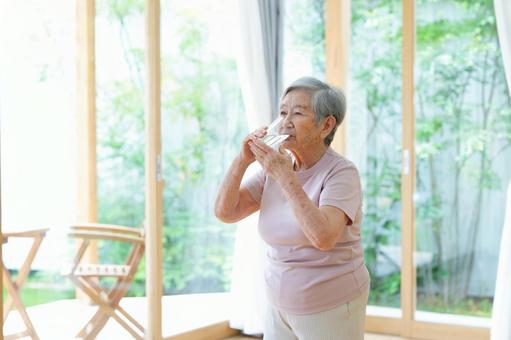 窓際に立ち水を飲む高齢女性 女性,水,飲むの写真素材