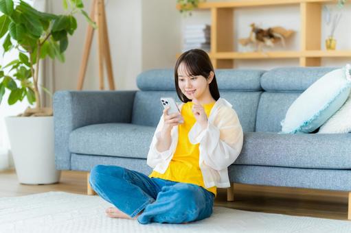部屋でスマホを操作する若い女性 部屋でスマホを操作する若い女性 スマホ,若い女性,笑顔の写真素材