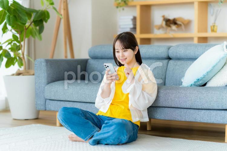 部屋でスマホを操作する若い女性 スマホ,若い女性,笑顔の写真素材