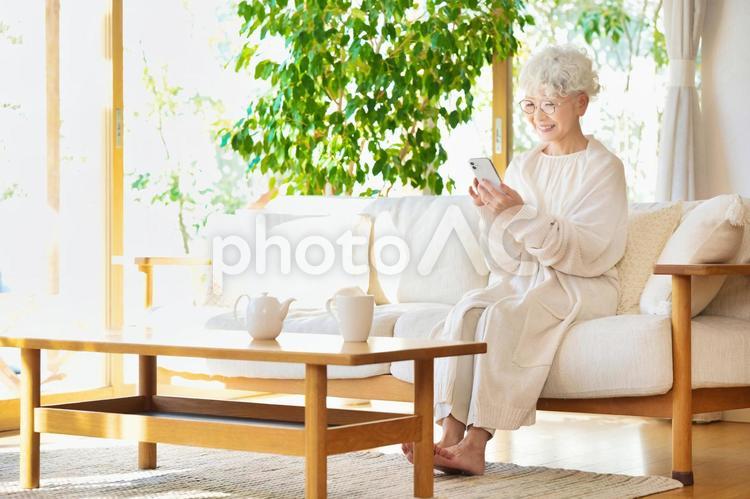 ソファーに座ってスマートフォンを使うシニア女性 女性,高齢者,おばあちゃんの写真素材