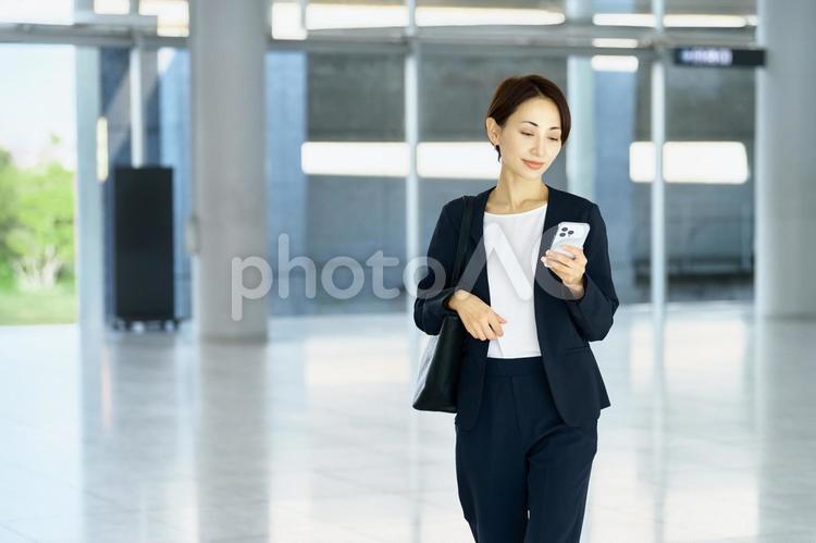 スマホを見るビジネスウーマン　歩く ビジネスウーマン,スマホ,笑顔の写真素材