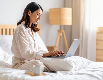 ベッドでノートパソコンを操作する女性の写真
