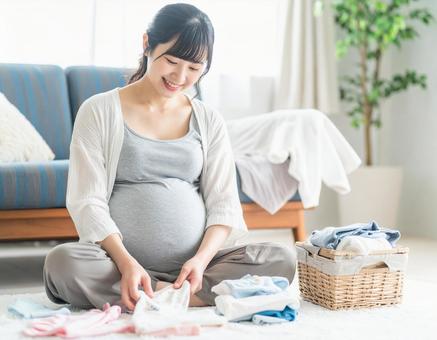 ベビー服を畳みながら微笑む妊婦の準備時間の写真