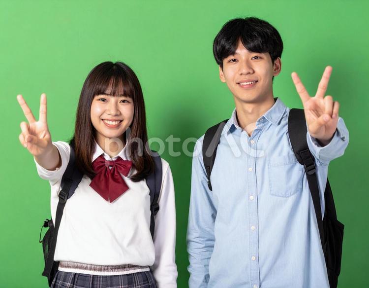 ピースサインをする高校生男女・緑背景 ピース,高校生,制服の写真素材