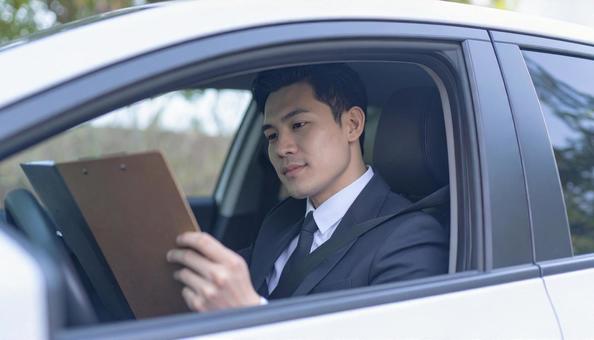 手もとに書類を持って運転するサラリーマンの写真