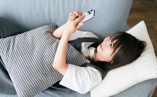 ソファに寝転んでスマホを使う女性 ソファに寝転んでスマホを使う女性 女性,スマホ,スマートフォンの写真素材