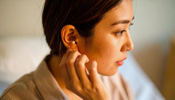 病室のベッドでピアスを外している女性患者 病室のベッドでピアスを外している女性患者の写真
