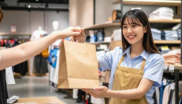 紙バックの商品を手渡す女性の店員の写真
