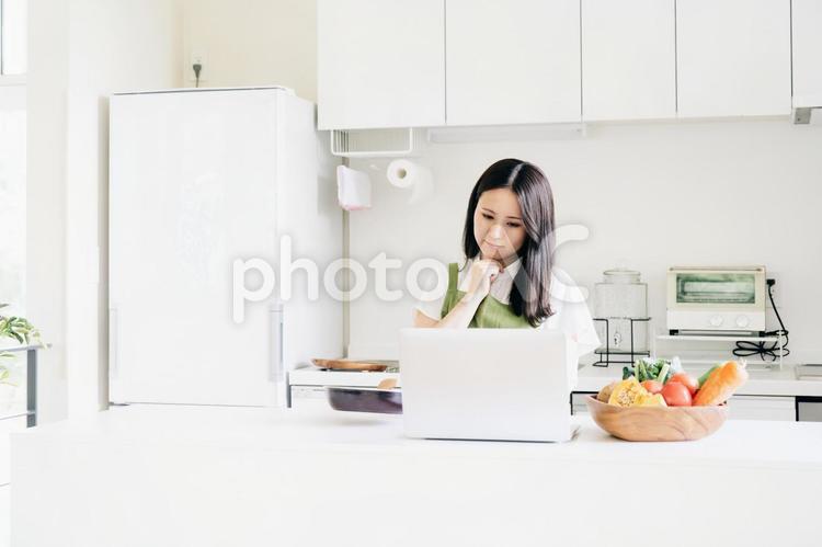 パソコンを見ながら料理する女性（困る） 料理,レシピ,家事の写真素材