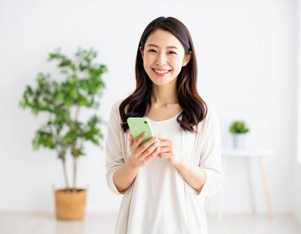 室内でスマートフォンを持つ笑顔の女性 室内でスマートフォンを持つ笑顔の女性の写真