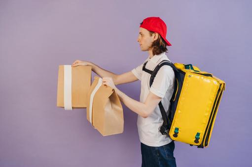 紙袋を渡すフードデリバリーの男性（紫背景）の写真