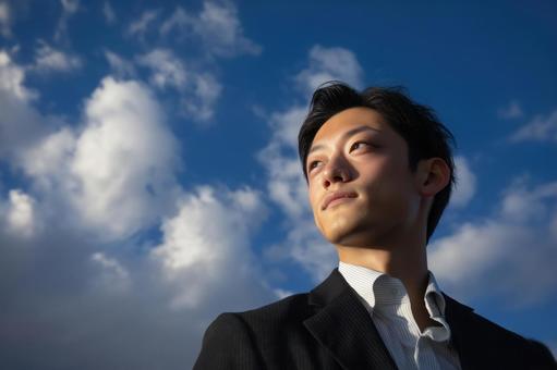 青空を見つめるスーツ姿の若い日本人男性 青空を見つめるスーツ姿の若い日本人男性の写真