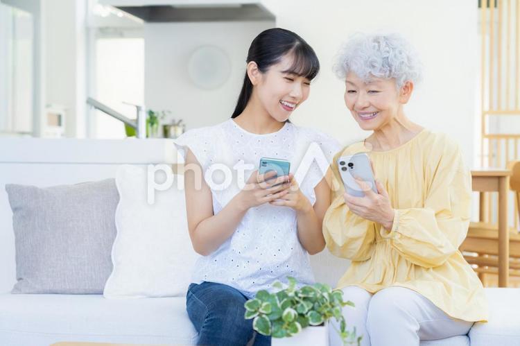 リビングスマホを見てくつろぐ孫と祖母 家族,シニア,女性の写真素材