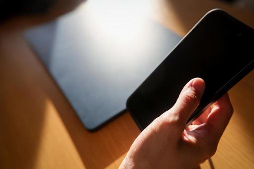 窓際でスマホとパソコンを操作する手 スマートフォン,スマホ,携帯電話の写真素材