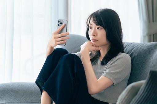 ソファに座ってスマホを使う女性 ソファに座ってスマホを使う女性 女性,スマホ,スマートフォンの写真素材