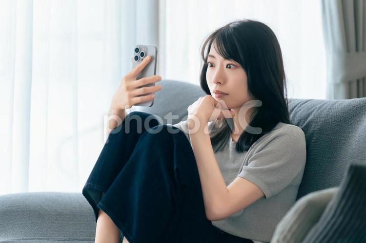 ソファに座ってスマホを使う女性 女性,スマホ,スマートフォンの写真素材