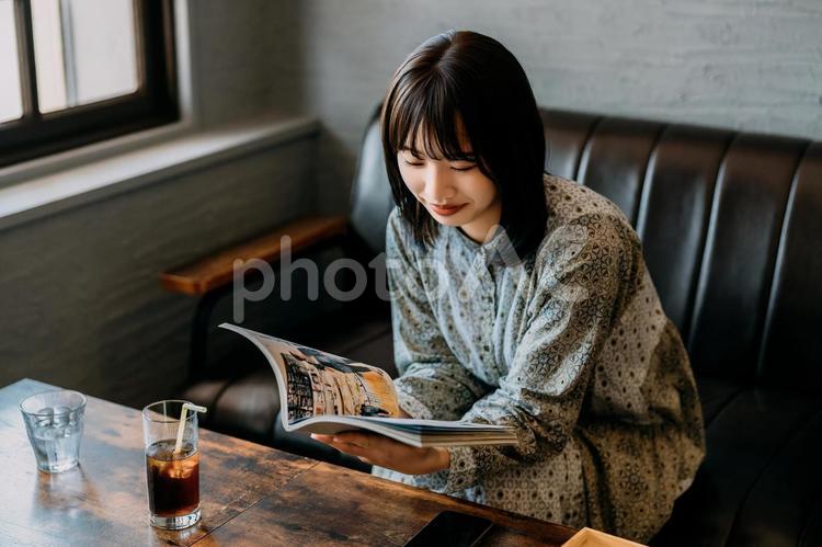 カフェのソファに座って雑誌を読む若い女性 女性,笑顔,本の写真素材