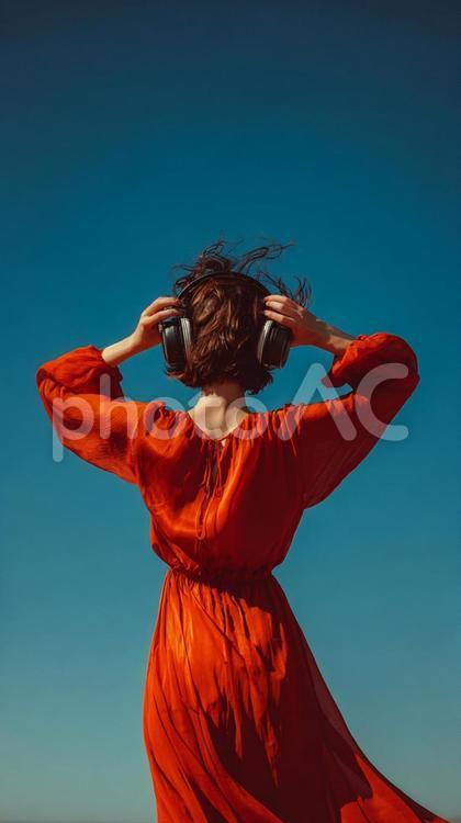 青空と赤いドレスの女性（後ろ姿） 女性,後ろ姿,ヘッドホンの写真素材