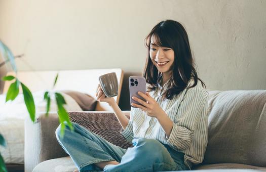 ソファでスマホを使う笑顔の女性 女性,スマホ,スマートフォンの写真素材