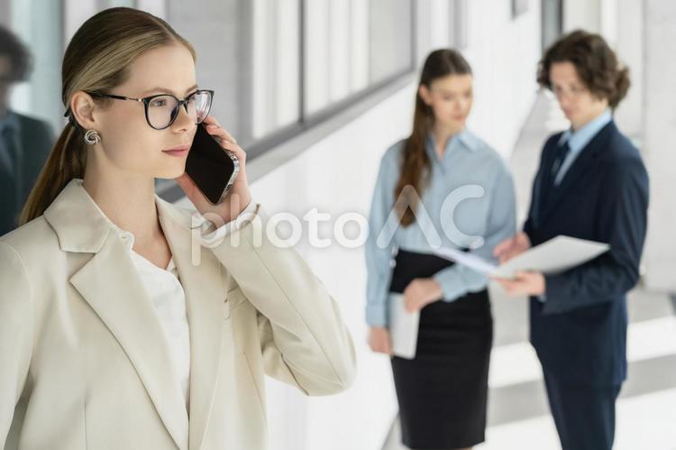 オフィスの廊下で立ち話する男女とスマートフォンで電話する女性 ビジネス,グループ,ビジネスマンの写真素材