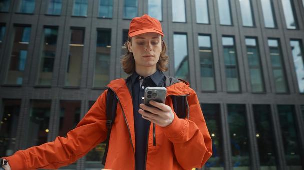 街なかでスマートフォンを使うるフードデリバリーの男性 配達,フードデリバリー,デリバリーの写真素材