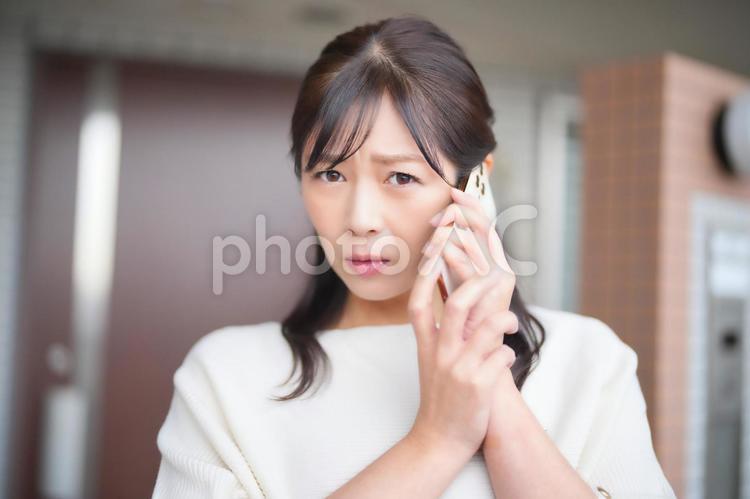 眉間にしわを寄せてスマートフォンで電話する女性 女性,主婦,眉間の写真素材