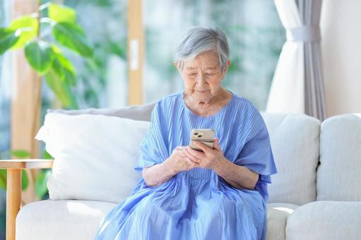 ソファでスマホを操作している高齢女性 女性,スマートフォン,持つの写真素材