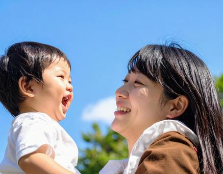 青空の下、子供を抱っこする母親 青空の下、子供を抱っこする母親の写真