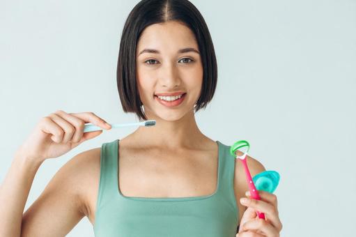 カメラ目線で歯ブラシを持ってベロクリーナーとフロスも持っている女性 カメラ目線で歯ブラシを持ってベロクリーナーとフロスも持っている女性の写真