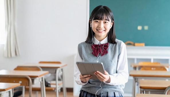 イヤホンをしてタブレットを見る女子学生 イヤホンをしてタブレットを見る女子学生の写真