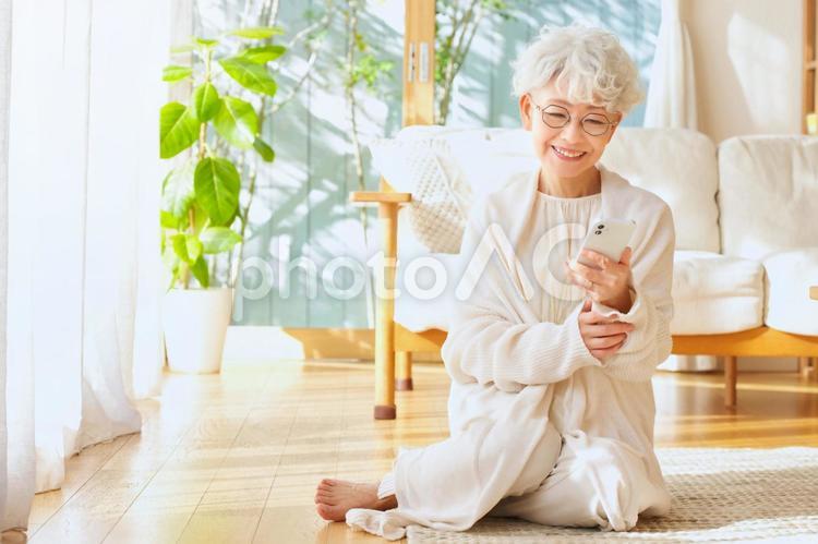 リビングの床に座ってスマートフォンを使うシニア女性 女性,高齢者,おばあちゃんの写真素材